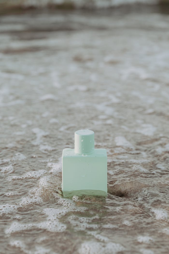 Minimalist perfume bottle resting on the sandy beach surrounded by ocean waves.